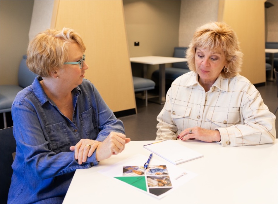 Two employees communicating at a table in office setting